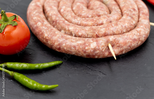 Raw sausage on a black background. Decorated with tomato and chili pepper.