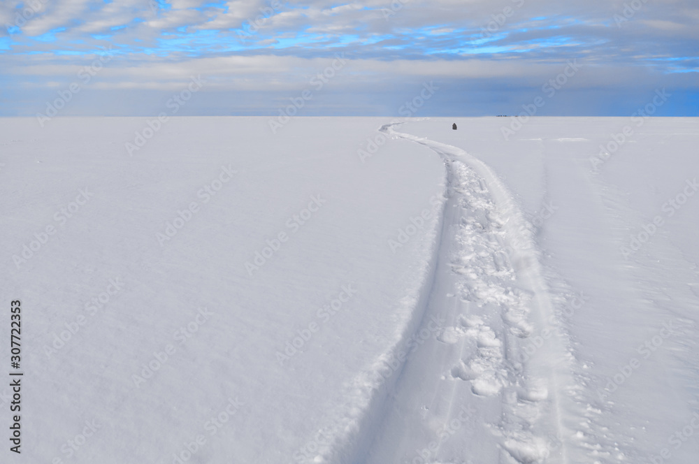 Path under a turquoise sky through a snowy field. The horizon between the sky and the snow field divides the frame in a ratio of one to four. You can place the text below. Path under a turquoise sky through a snowy field. The horizon between the sky and the snow field divides the frame in a ratio of one to four. You can place the text below.