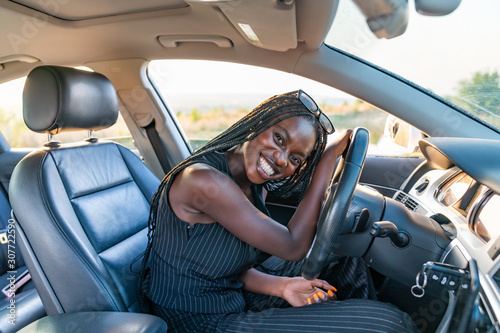 Happy smiling african girl in black striped clothes is driving a car