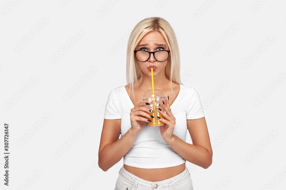 Funny cute attractive careless blonde woman is drinking cocktail in a plastic cup using a straw, isolated on white background. So delicious. Sexy smiling girl with juice. Funny cute attractive careless blonde woman is drinking cocktail in a plastic cup using a straw, isolated on white background. So delicious. Sexy smiling girl with juice.