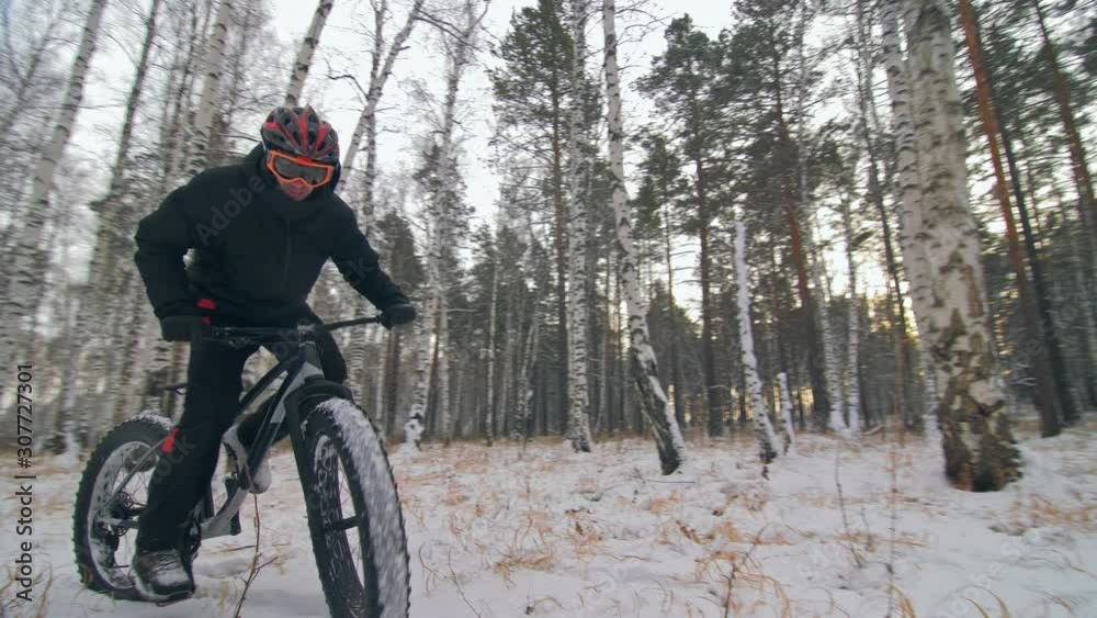 Professional extreme sportsman biker riding fat bike in outdoors. Cyclist ride in winter snow forest. Man does trial trick pedal kick jump on mountain bicycle with big tire in helmet and glasses. Professional extreme sportsman biker riding fat bike in outdoors. Cyclist ride in winter snow forest. Man does trial trick pedal kick jump on mountain bicycle with big tire in helmet and glasses.
