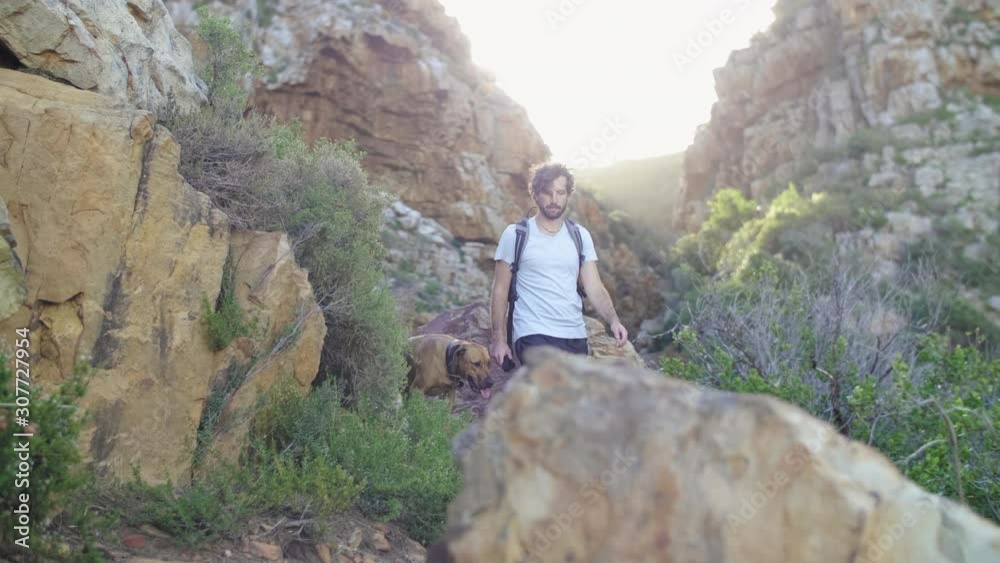 Young active man walking his pet dog in nature reserve, rocky canyon path in ravine at sunset Young active man walking his pet dog in nature reserve, rocky canyon path in ravine at sunset