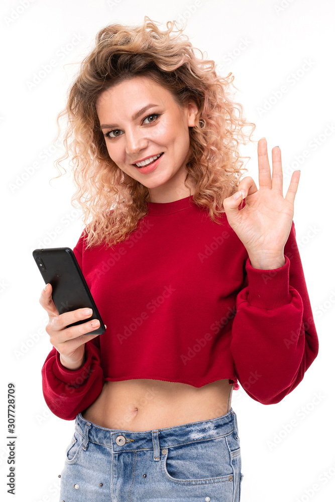 smiling curly blonde girl with a phone in his hand on a white background