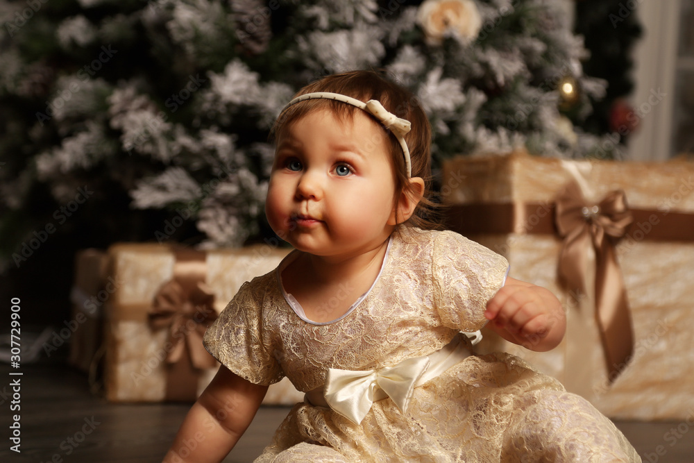 a little, beautiful girl, receives gifts for Christmas,and makes a wish near the Christmas tree in a beautiful gold dress