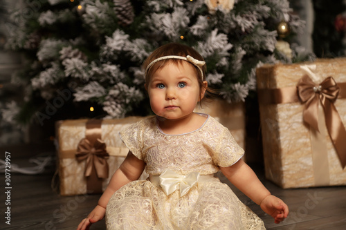 a little, beautiful girl, receives gifts for Christmas,and makes a wish near the Christmas tree in a beautiful gold dress