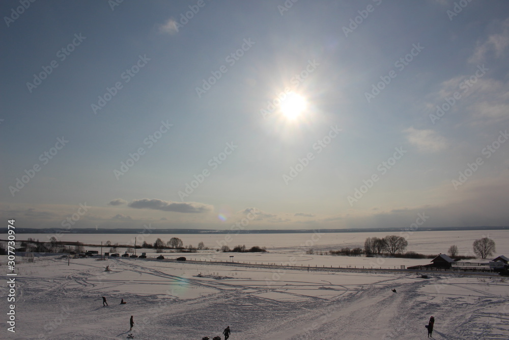 winter frosty landscape, blue sky with clouds, white snow, house field and sun in winter. riding the hills on sleds.