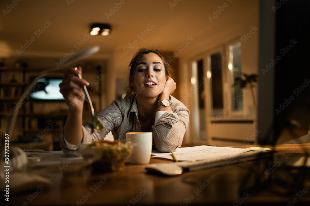 Female student eating salad while studying at night at home. Female student eating salad while studying at night at home.