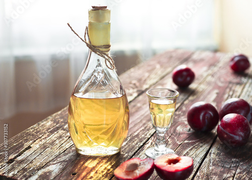 Traditional Balkan plum brandy - rakija or rakia slivovica in the bottle, a wineglass with sljivovica and fresh plums on the wooden background in dayligt. photo