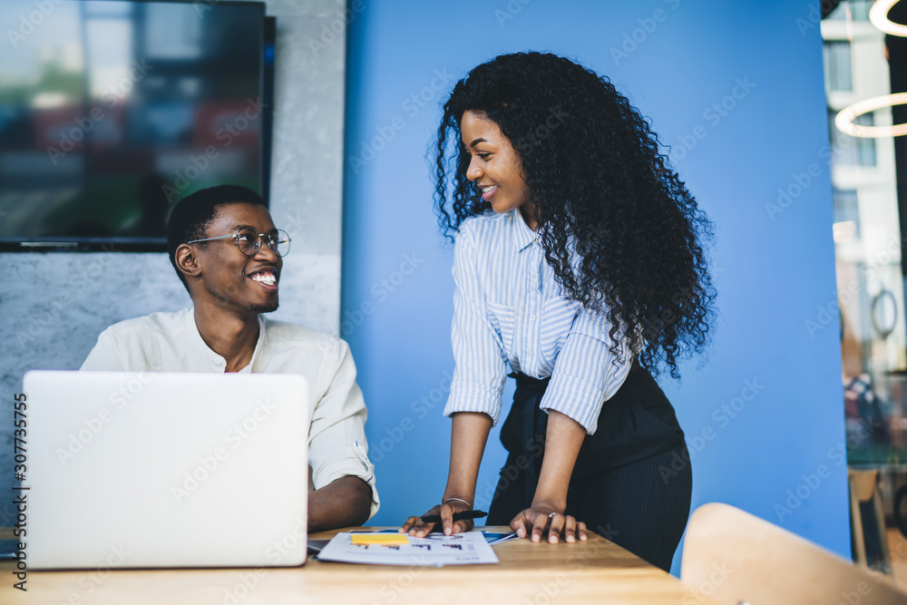 Smiling coworkers preparing report and browsing laptop in office Smiling coworkers preparing report and browsing laptop in office
