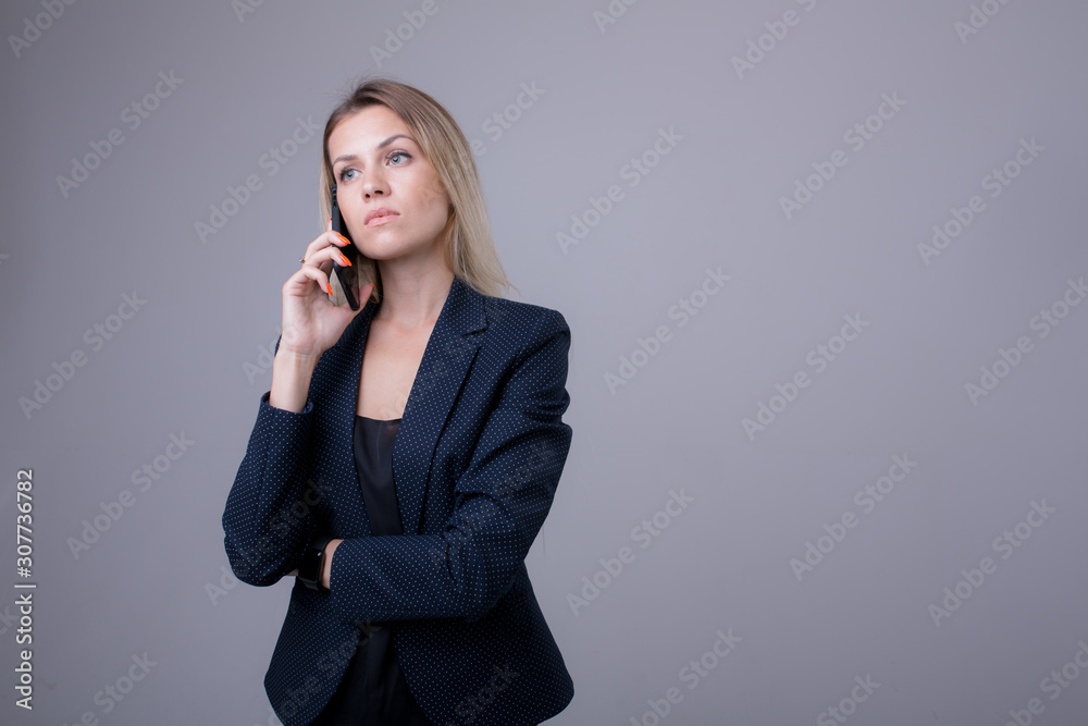 blonde business lady agrees on the phone with the customer in a blue jacket on a gray background and smiles blonde business lady agrees on the phone with the customer in a blue jacket on a gray background and smiles