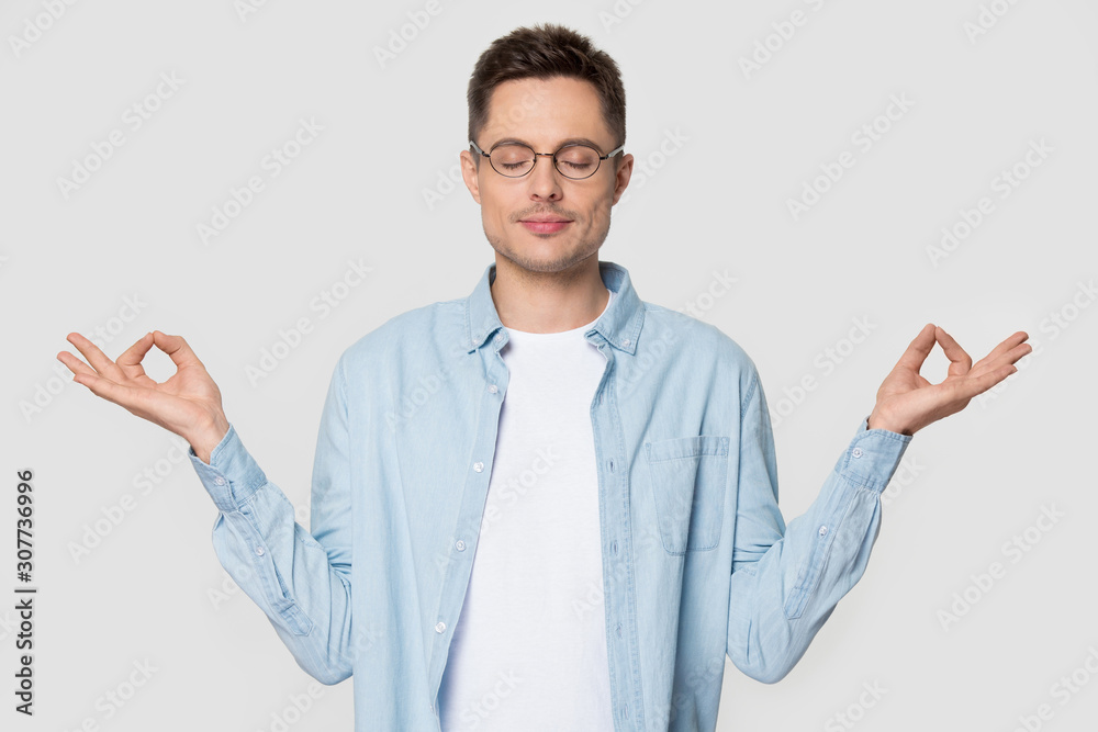 Relaxed millennial man standing meditating at studio with eyes closed Relaxed millennial man standing meditating at studio with eyes closed