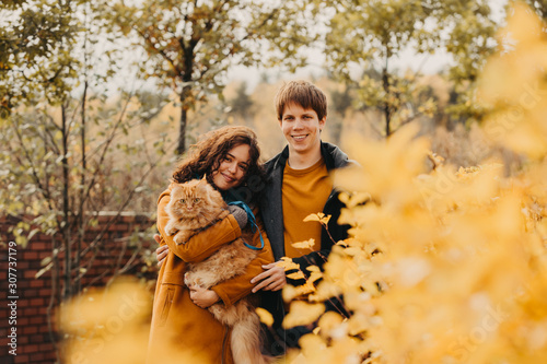 Young couple with a red cat on a background of an autumn park.