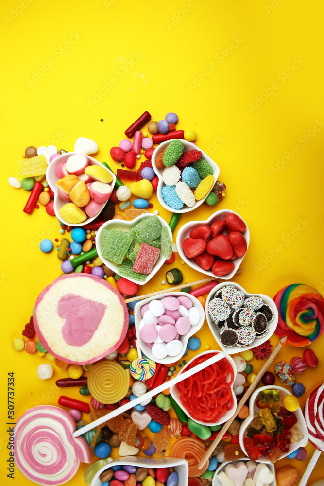 candies with jelly and sugar. colorful array of different childs sweets and treats on yellow background