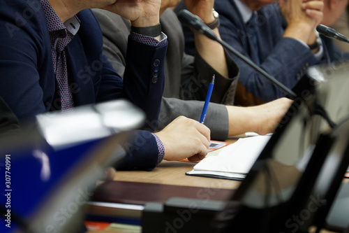 Participants in a business meeting with notebooks, pens, watches, and monitors carefully listen to the speaker. Work time. Business style. Close-up photo