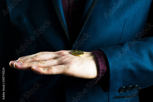 A businessman in a purple suit holds a yellow coin in the palm of his hand.