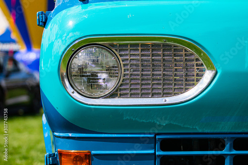 Turquoise blue old classic antique American car half front, left side, close up and selective focus on glass headlight with metallic chrome frame © Valmedia