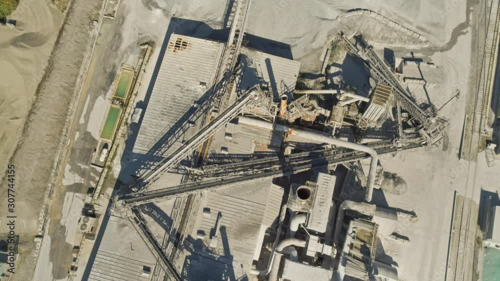 Drone, aerial, bird's eye view, medium wide shot of a factory, camera tilts up to show a river and a bustling city. Camera then steadies for a wide shot.
