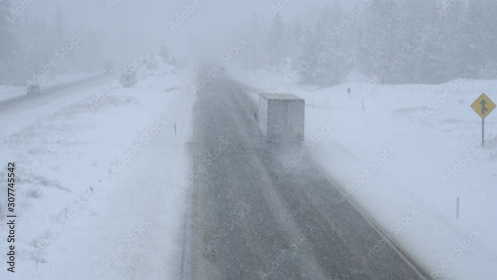 Cargo trucks and cars make their way through an intense blizzard along a dangerous country road leading through pine woods in Washington. Stunning shot of traffic moving through a bad snowstorm. Cargo trucks and cars make their way through an intense blizzard along a dangerous country road leading through pine woods in Washington. Stunning shot of traffic moving through a bad snowstorm.