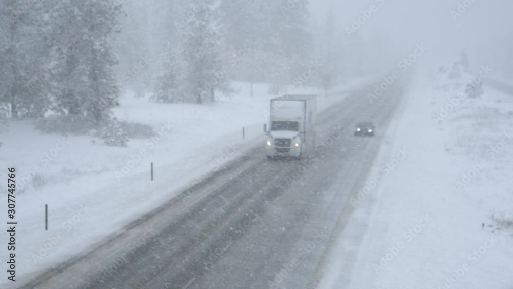 Semi-truck and car drive along snowy country road in horrible weather conditions. Two vehicles carefully navigate the interstate road during a blizzard. People driving across state in poor visibility. Semi-truck and car drive along snowy country road in horrible weather conditions. Two vehicles carefully navigate the interstate road during a blizzard. People driving across state in poor visibility.