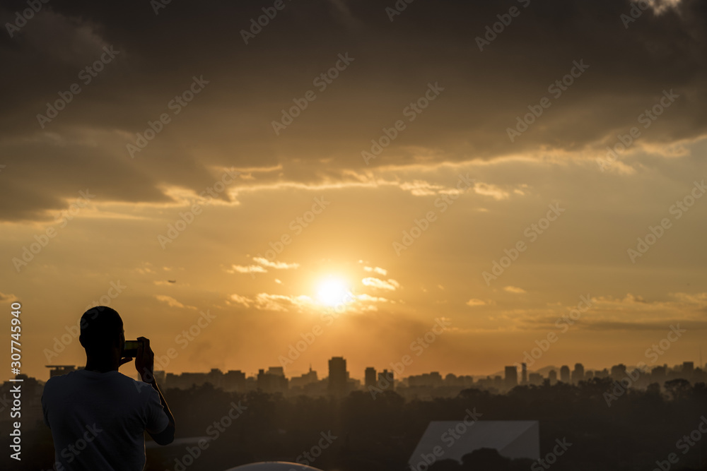 Homem fotografa o pôr do sol na cidade de São Paulo, Brasil