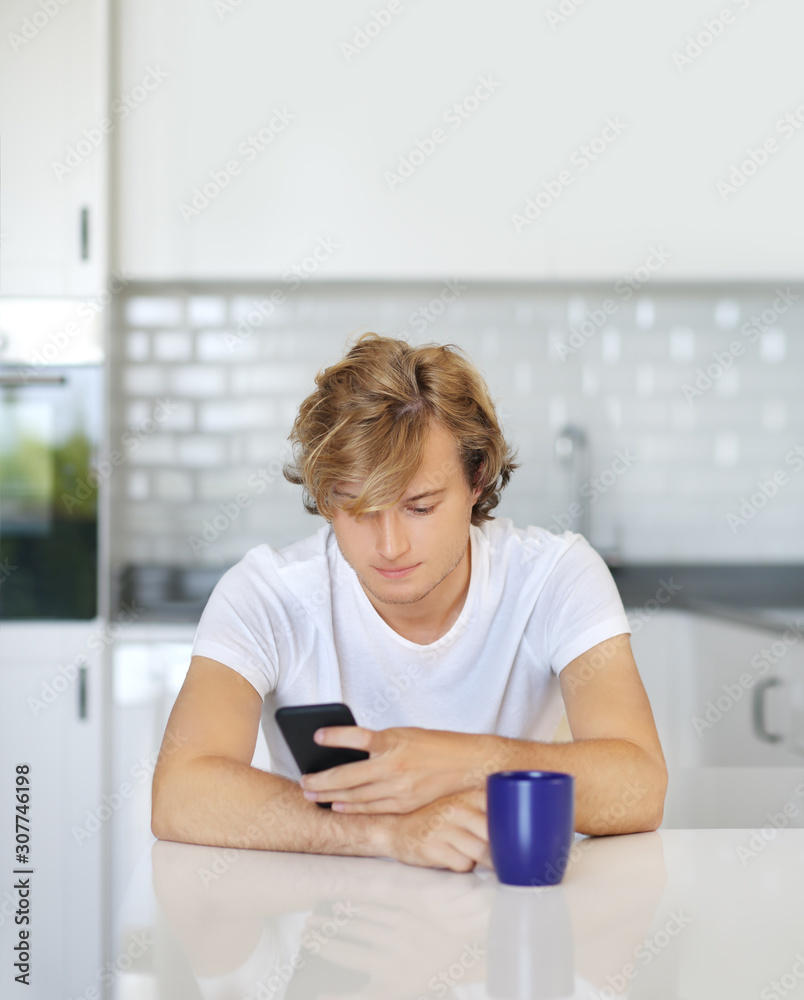 Teenage boy typing text message.Sitting in the kitchen.Using smart phone Teenage boy typing text message.Sitting in the kitchen.Using smart phone