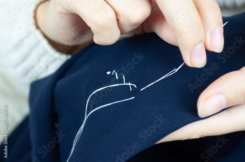 Woman's fingers with thread and needle stitching fabric. Hands sewing, repairing clothes Tailoring and homecraft concept