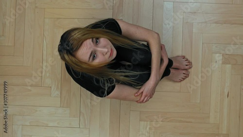 Sad woman sitting on floor and looking to camera. She is lonely and depressed.