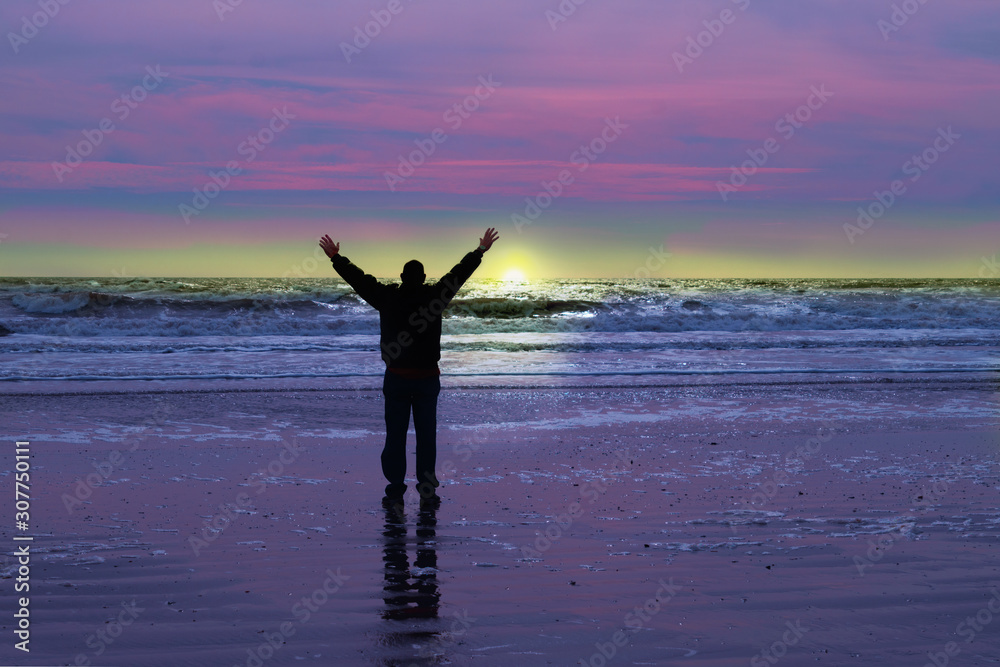 Concept of a man  joyously greeting dawn alone on a beach.