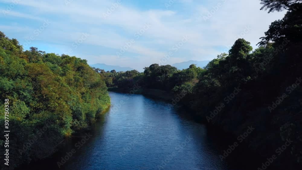 Low aerial shot going up revealing beautiful scenery river in tropical green forest with mountains in background Low aerial shot going up revealing beautiful scenery river in tropical green forest with mountains in background