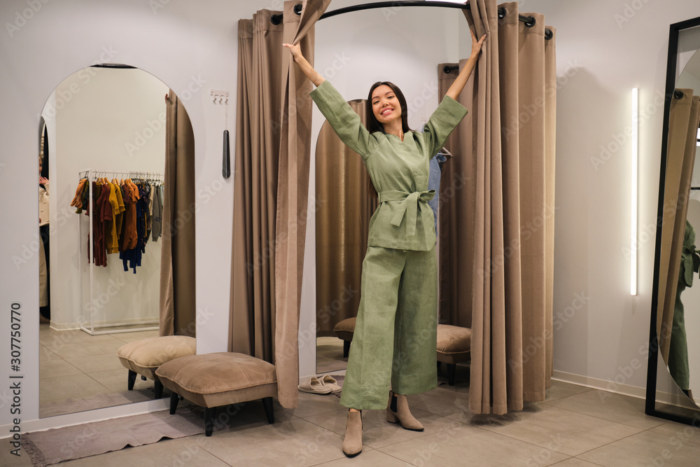 Beautiful smiling Asian girl trying on stylish suit in dressing room of clothes store