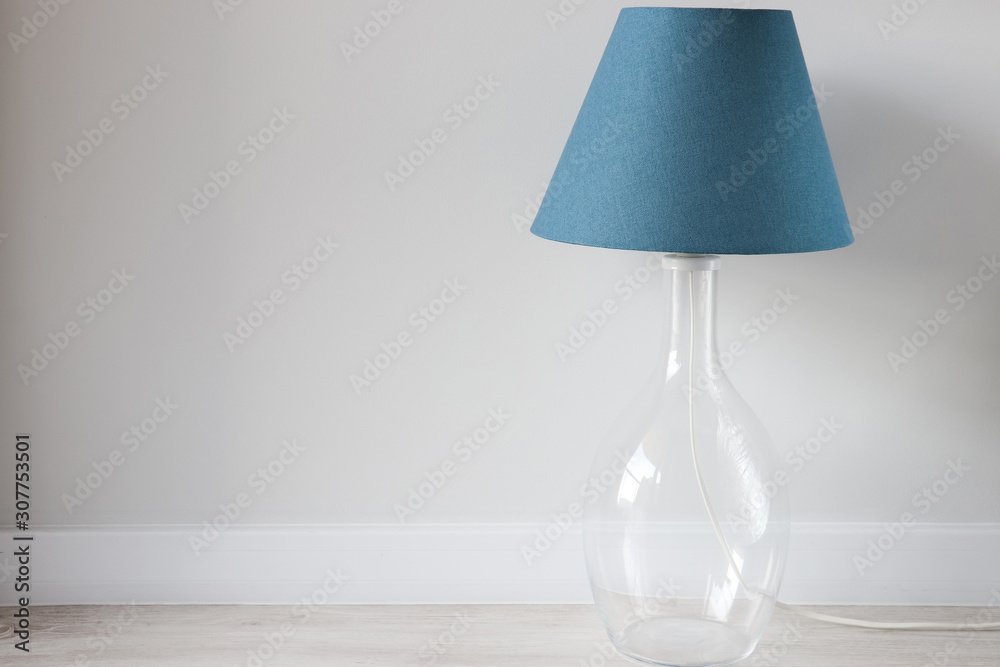 Blue lampshade on the table lamp with glass element near the light wall. Trendy color in your interior. Blue lampshade on the table lamp with glass element near the light wall. Trendy color in your interior.