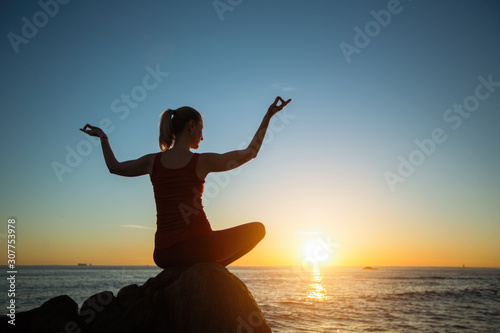 Yoga silhouette of young woman on the sea beach at amazing sunset.