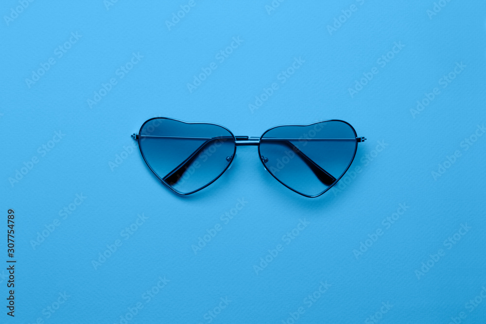 Fototapeta premium Bright blue heart-shaped glasses on a paper background.