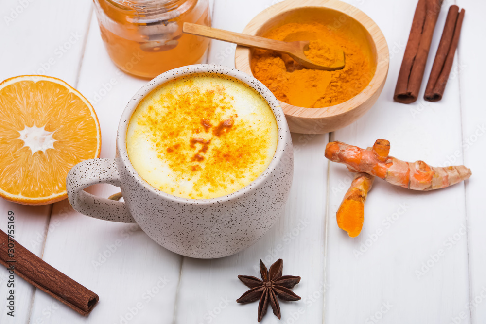 Detox turmeric tea golden milk and ingredients on white wooden table