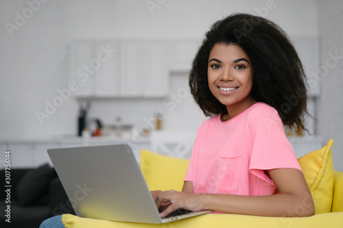 African American woman using laptop computer and internet, shopping online, ordering food, booking tickets,  sitting at home. Happy student studying, learning language, online education concept  © Oleksii