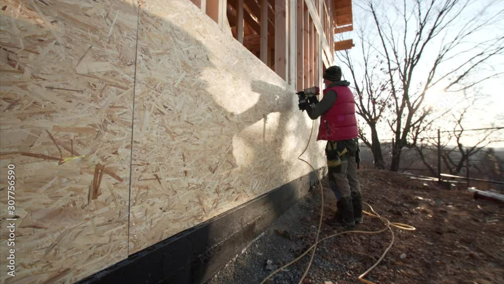 Professional builder is hammering nails in plywood with hydraulic hammer. Wooden frame residential house under construction Professional builder is hammering nails in plywood with hydraulic hammer. Wooden frame residential house under construction