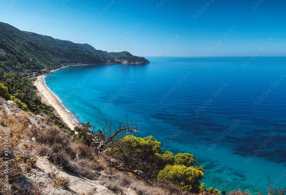 Beautiful turquoise color of sea water is seen through the foliage of trees on Pefkoulia Beach, Lefkada island, Greece. Idyllic sunny day.