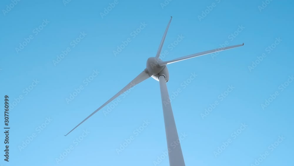 Slow motion of the blades of a large wind turbine in a field against a blue sky on a sunny summer day. View from the bottom up. Alternative energy sources. Wind park. Ecological energy. Industrial Slow motion of the blades of a large wind turbine in a field against a blue sky on a sunny summer day. View from the bottom up. Alternative energy sources. Wind park. Ecological energy. Industrial