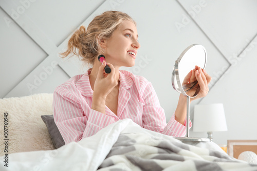 Morning of beautiful young woman applying makeup in bedroom