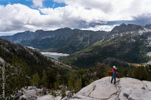 A backpacker looks out across a vast sweeping view of lakes and mountains from the top of a rocky bluff