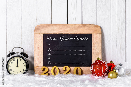 2020 wooden text with Alarm clock with Christmas ornaments and New Year's Goals List written on chalkboard with white fur