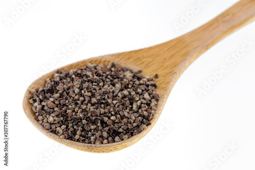 Spoon full of ground black pepper on a white background