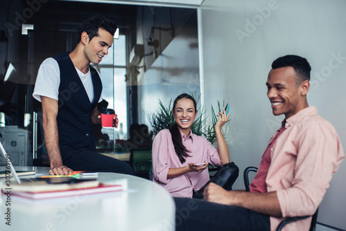 Prosperous business marketers sitting at desktop in coworking space and laughing during working time discussing collaboration and teamwork, joyful crew of analytic experts rejoicing and joking indoors