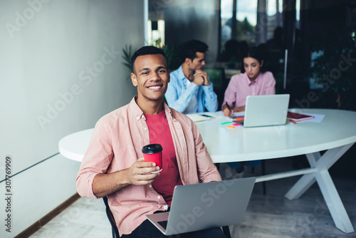 Smiling man surfing on laptop and drinking coffee in office