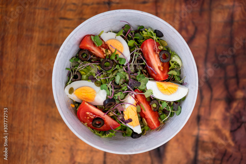 Healthy vegetable salad with mixed green leaves (arugula, mesclun, lettuce), eggs, black olives, tomato and bean sprouts. Wooden background. Top view