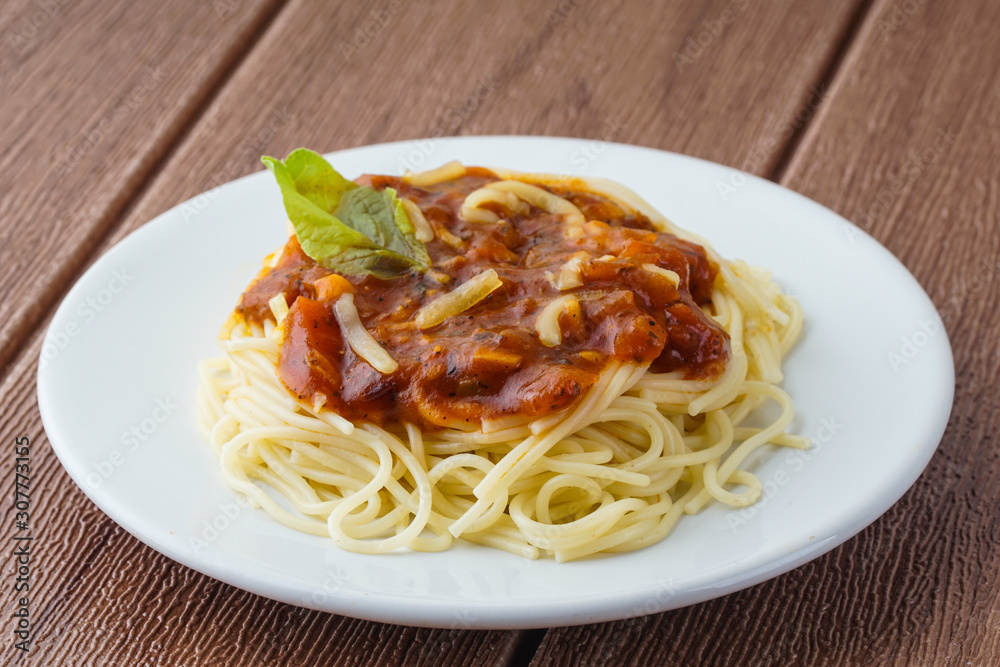 View of spagetti bolognese with green basil on white plate over brown background