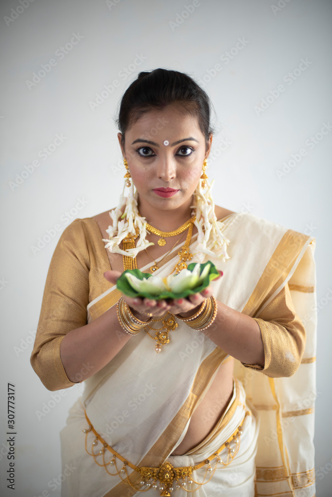 Portrait of an young and attractive Indian  woman in white traditional wear with colorful flowers in hands   for the celebration of Onam/Pongal in white background. Indian lifestyle.