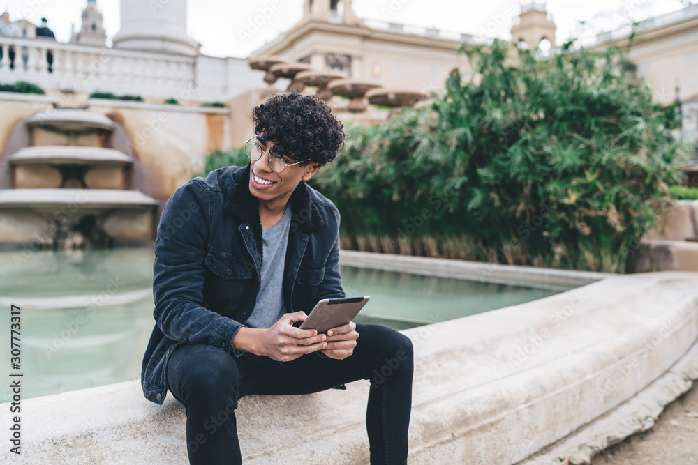 Black man with tablet sitting on side of fountain smiling