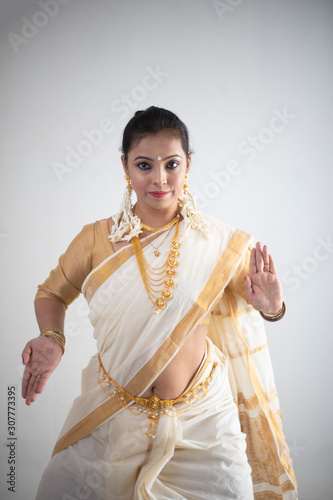 An young and attractive Indian  woman in white traditional wear dancing traditional dance form for the celebration of Onam/Pongal in white background. Indian lifestyle.