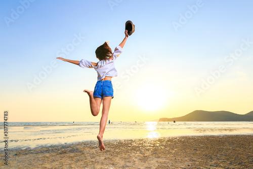 travel women hold hat and jump on the beach.